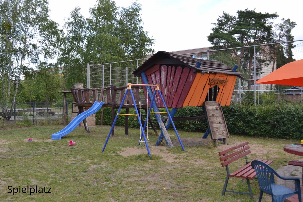 Blick auf den Spielplatz im Garten des Dietrich-Bonhoeffer-Hauses mit einer Rutsche und einer Schaukel.